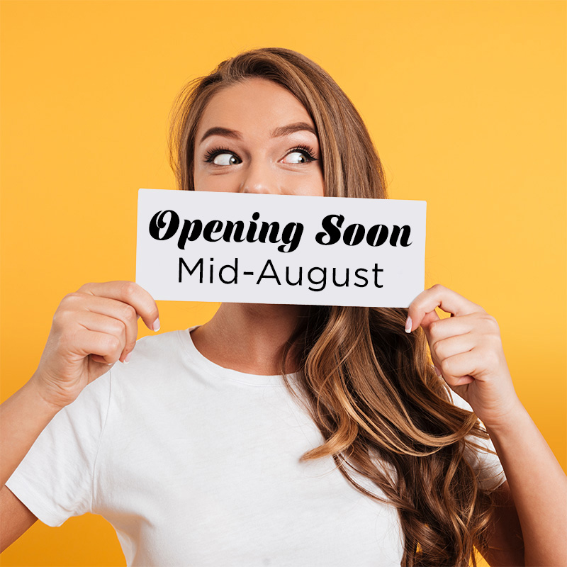 A woman holding a sign that says "Opening Soon, mid august"